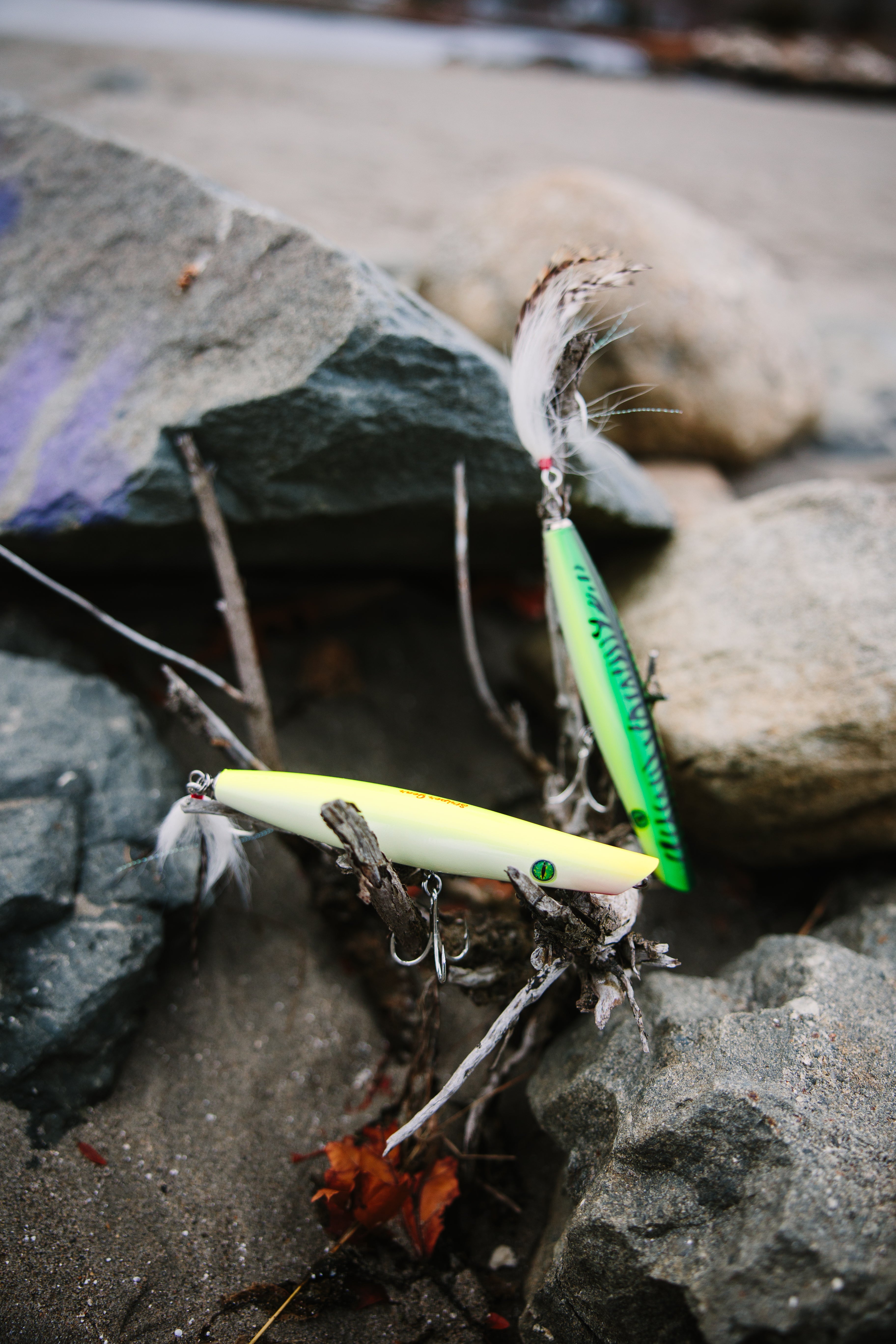 Two pencil popper fishing lures on a rocky surface with blurred background