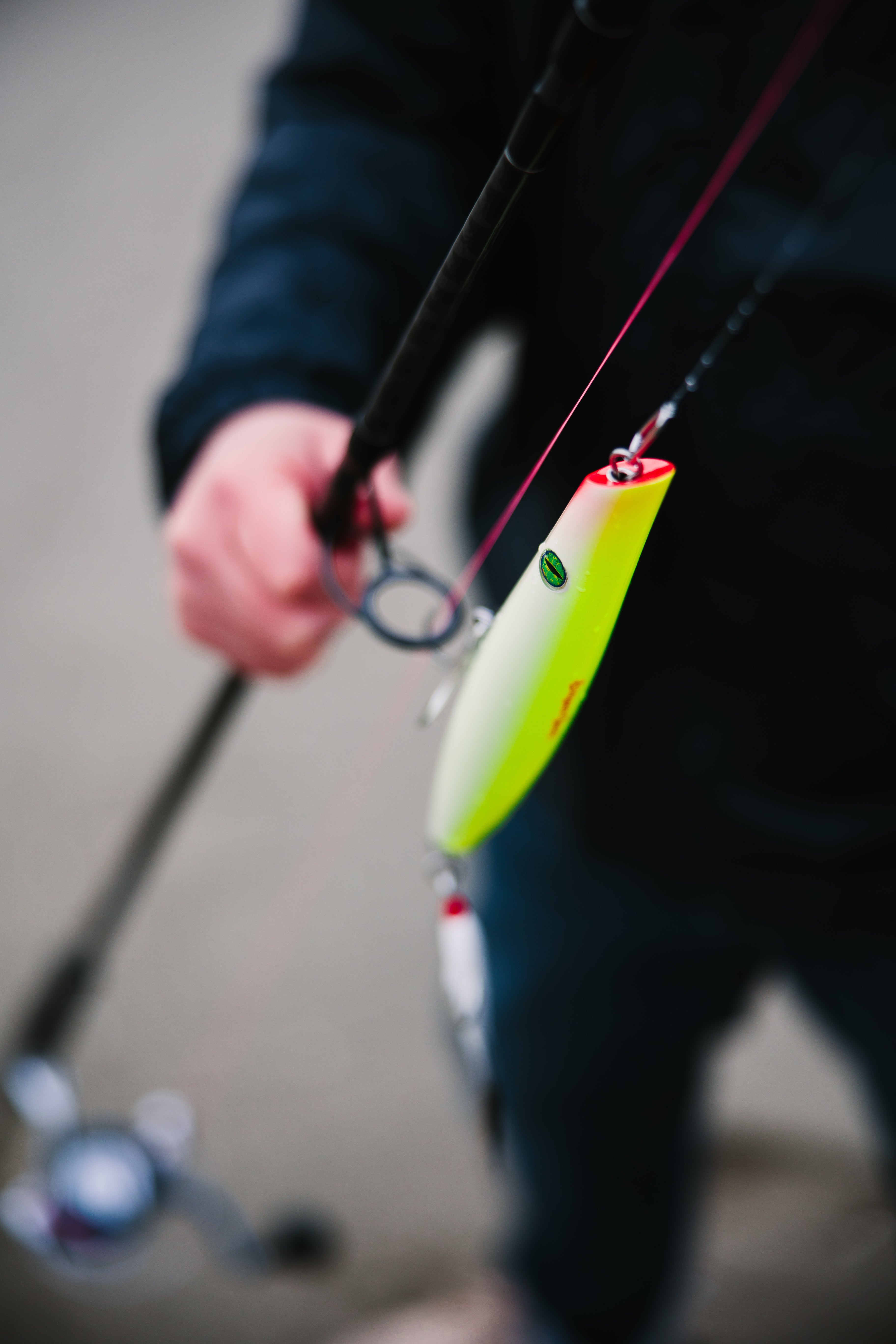 Close-up of a fishing rod with a bright yellow pencil popper lure held by a person.