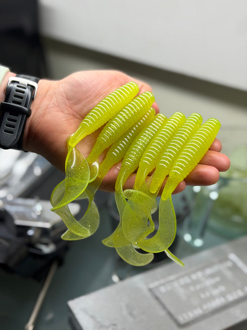 Hand holding yellow soft plastic fishing lures with a blurred background
