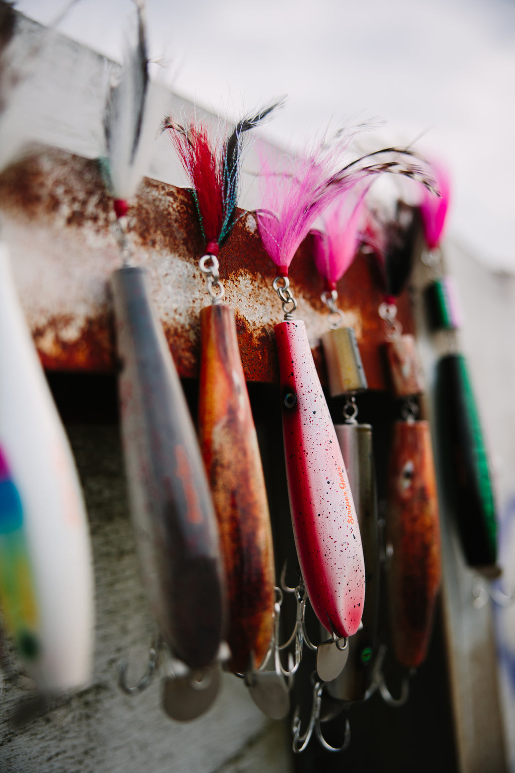 Close-up of metal lip fishing lures with feathers on a rusty metal beam.