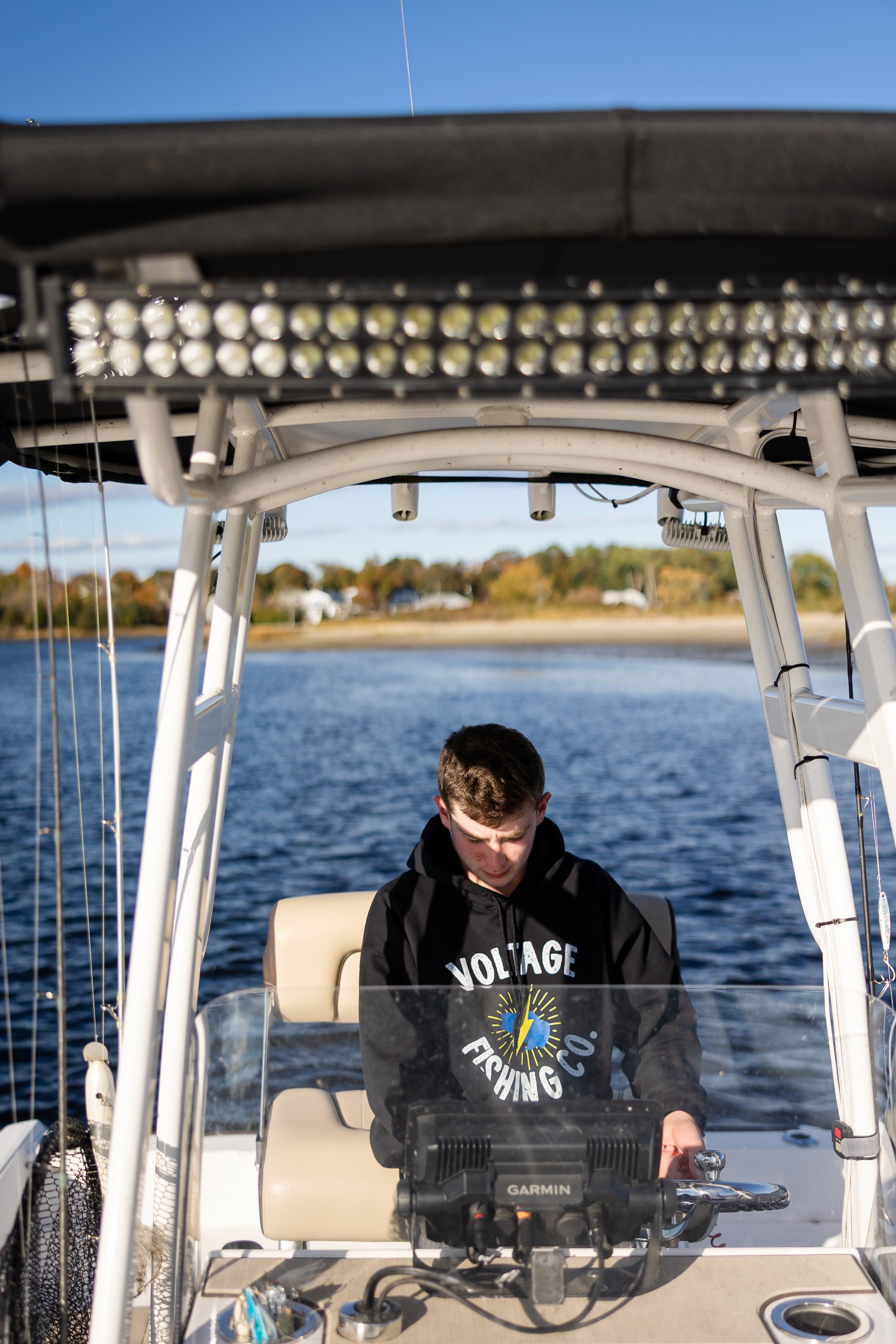Person on a boat, wearing a Voltage Fishing Co. sweatshirt, using a fish finder.